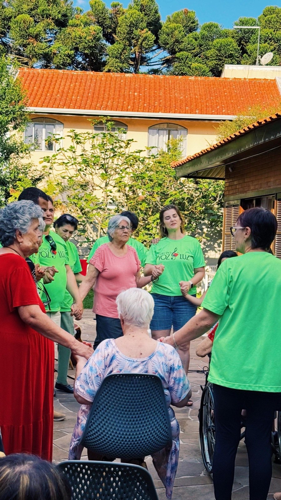 Residentes e equipe de mãos dadas em roda de atividade no jardim da casa de repouso